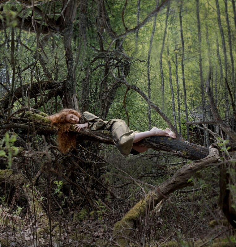Tiheässä metsässä lepää nainen kietoutuneena puoliksi kaatuneeseen puunrunkoon.